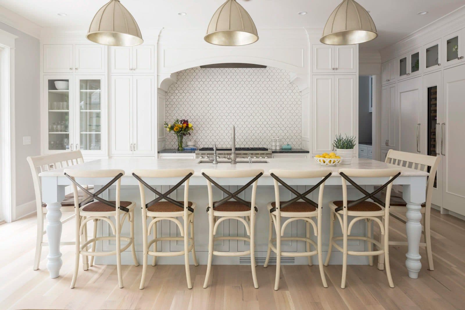 Transitional white kitchen with gold pendants, marble island, and arabesque tile backsplash